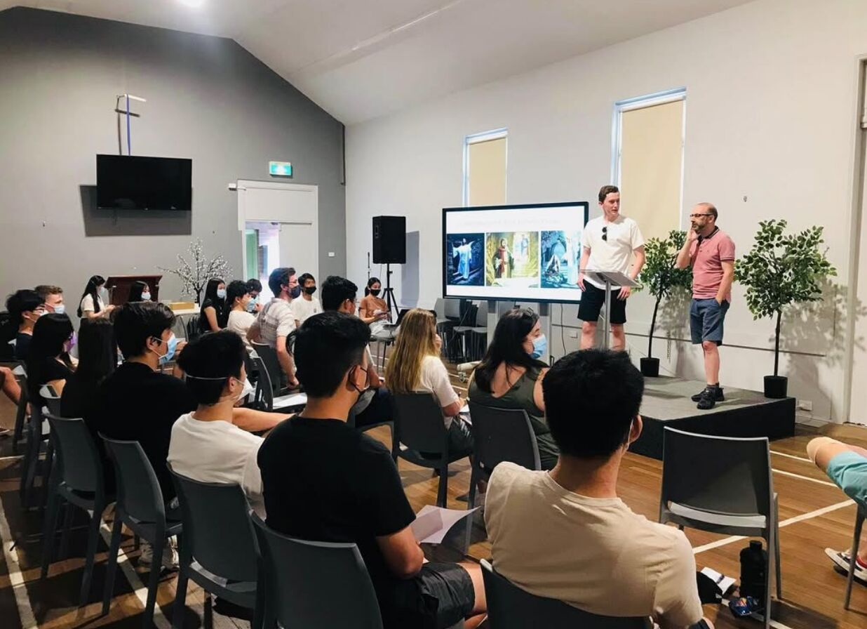 Two leaders giving a talk with slides to grads seated in a church hall