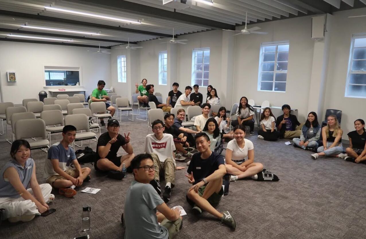 Grads sitting on the floor of a church hall at Connect, smiling and waving at the camera