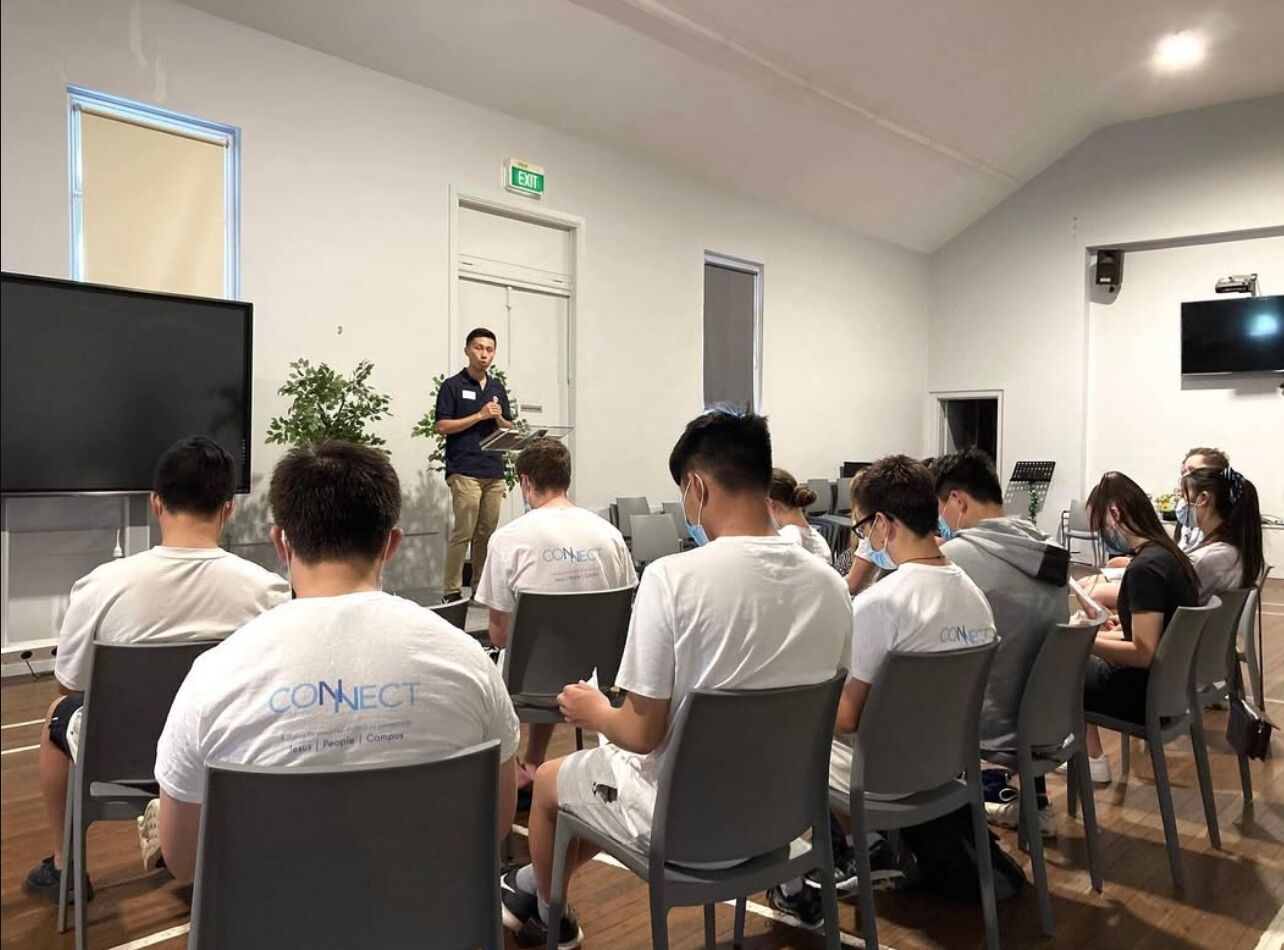 A Connect leader giving a talk to grads in Connect t-shirts, seated in a church hall