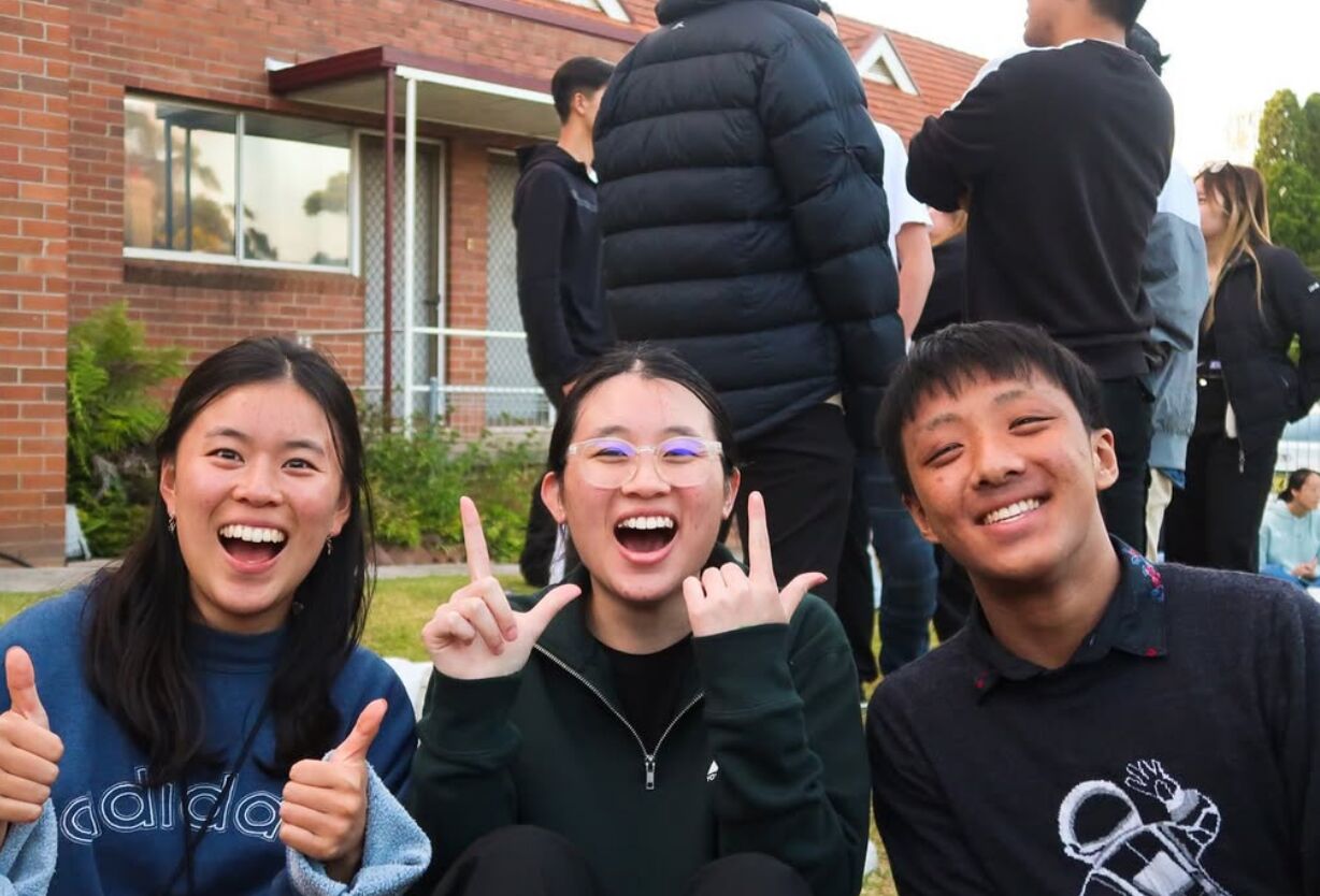 Three grads grinning at the camera, giving thumbs up