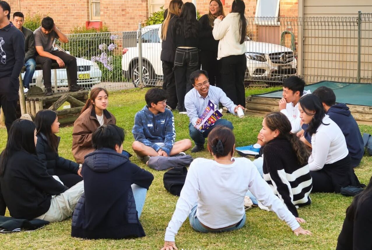 A leader chatting with a circle of grads sitting on the grass