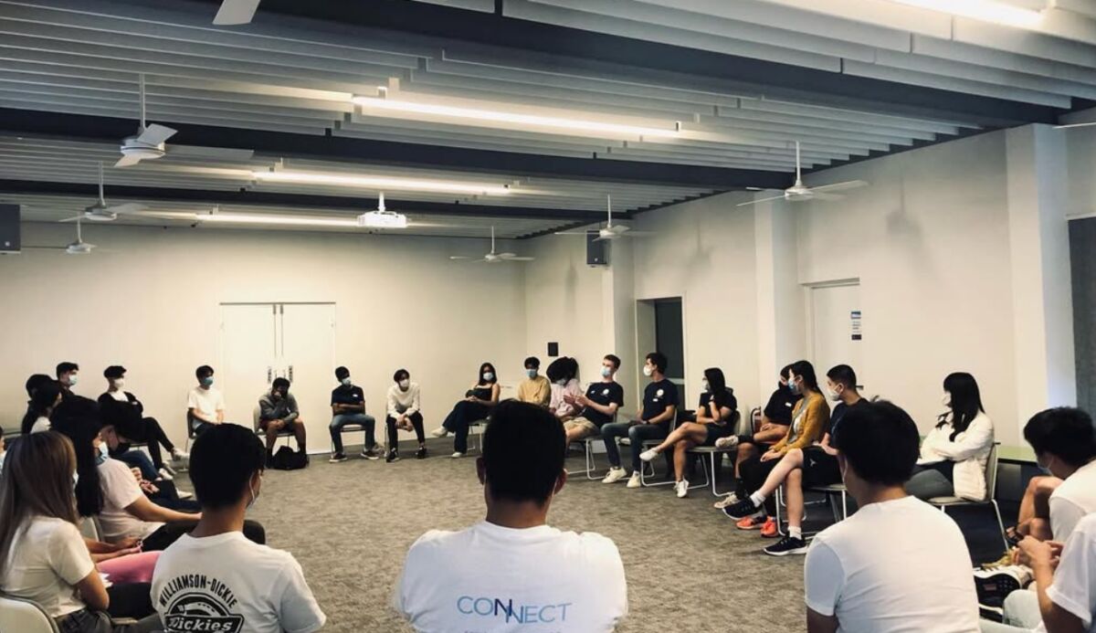 Grads in Connect t-shirts sitting in a big circle, talking together in a hall